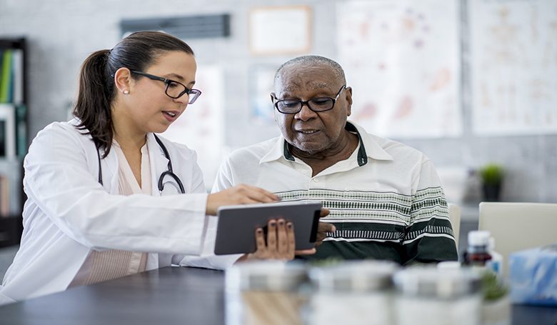 Doctor With A Tablet Computer A senior man of African descent is indoors in a hospital room. He is watching his female doctor using a tablet computer. She is explaining a medication schedule to him.