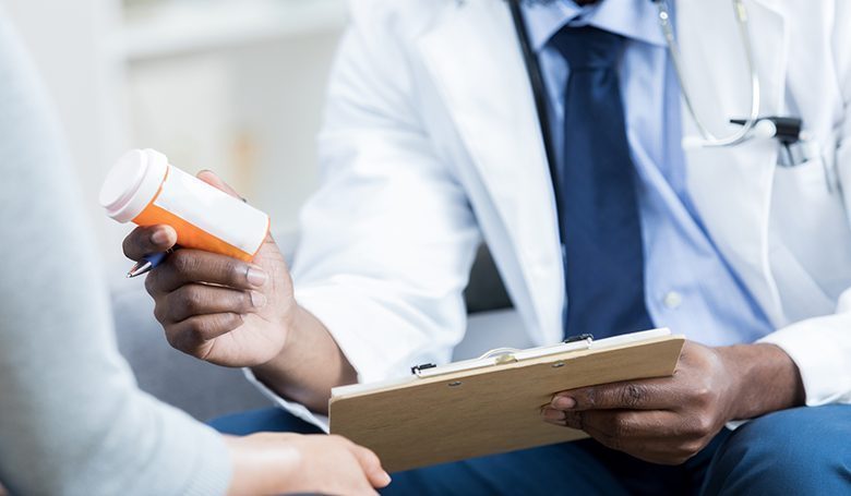 Unrecognizable doctor gives patient prescription medication African American doctor hands a prescription medication bottle to a female patient. The doctor is holding the patient's chart.